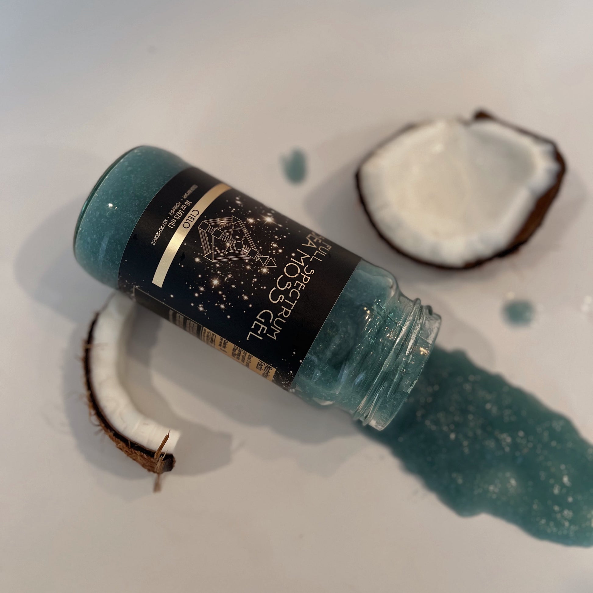 Organically Kismet Cielo Sea Moss Gel spilled from a bottle onto a clean surface, surrounded by fresh coconut pieces with its blue-green gel shimmering in soft light.