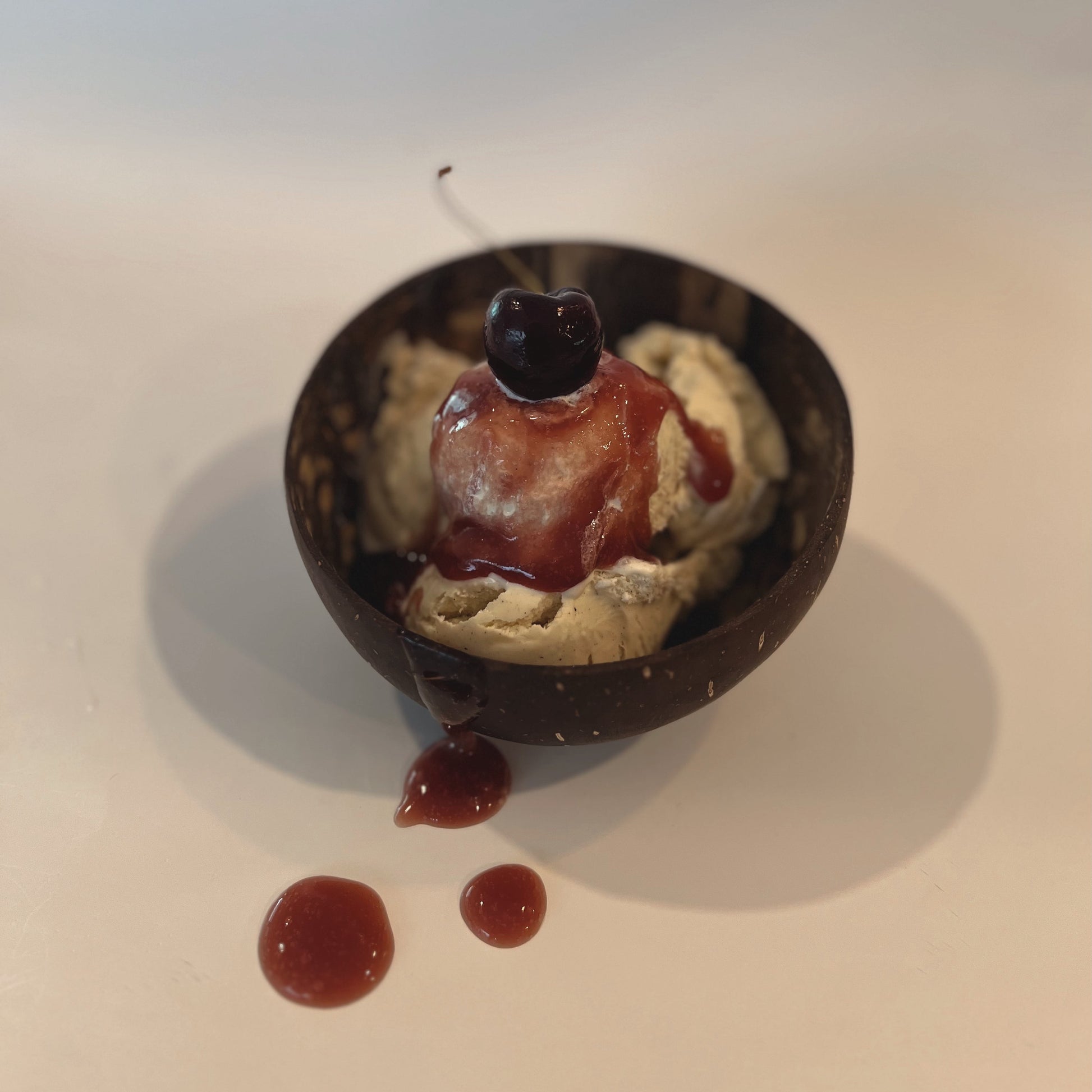 Immuniberry full spectrum sea moss gel drizzled over ice cream in a dark bowl, topped with cherries, showcasing texture and richness.