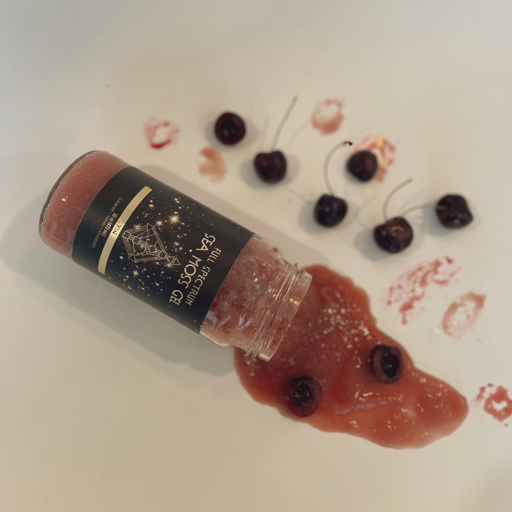Organically Kismet Yin Sea Moss Gel spilled with whole cherries and cherry puree on a white surface, showcasing its rich color and natural ingredients.
